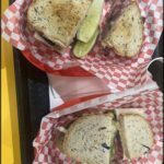 Two sandwiches are cut in half and placed on a red and white checkered napkin.
