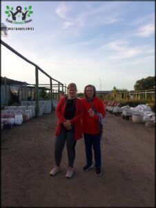 two women standing in a dirt field with bags of food