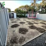 A backyard with a swing set and a dirt area with holes in it.