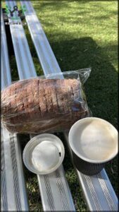 A bag of bread sits on a table next to a cup of coffee.