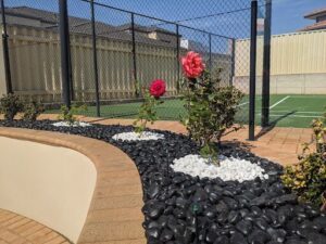 A beautiful garden with a variety of flowers, including red roses, is situated in front of a building.