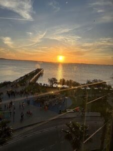 A beautiful sunset over the ocean, with a pier and a beach filled with people enjoying the view.