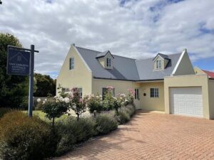 A beautiful white house with a gray roof and a garden of flowers in front of it.