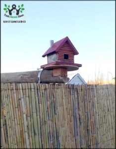 A birdhouse is perched on a wooden post, surrounded by a fence.