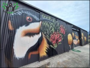 A black and white bird with a red flower in its mouth is painted on a building.
