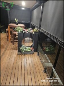 A black planter with flowers sits on a wooden deck.