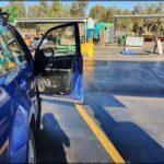 A blue car is parked in a parking lot, with its door open.