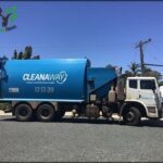 A blue dump truck with the words "cleanaway" on the side is parked on the side of the road.