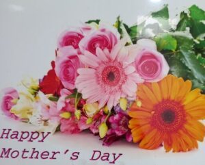 A bouquet of flowers is displayed on a table, with a card that reads "Happy Mother's Day."