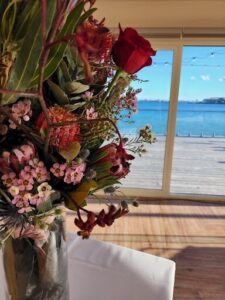 A bouquet of flowers sits on a table, overlooking a beautiful ocean view.
