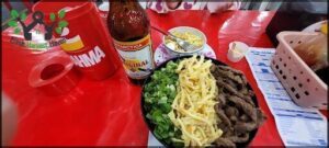A bowl of food sits on a table next to a bottle of beer.