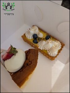 A box of desserts, including a chocolate cake and a blueberry pastry, is displayed on a table.