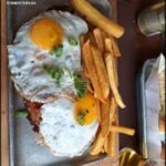 A breakfast plate with eggs, fries, and a drink.