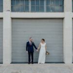 A bride and groom stand in front of a garage door, posing for their wedding photos.