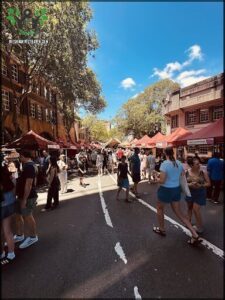 A bustling street scene with people walking and standing, and a large crowd of people gathered in a marketplace.