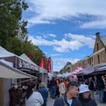 A bustling street scene with people walking around and shopping at various outdoor stands.