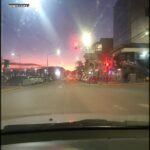 A car is driving down a street at dusk, with a red stoplight visible in the distance.
