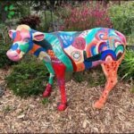 A colorful cow statue is displayed in a garden setting.