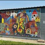 A colorful mosaic of a cityscape is displayed on the side of a building.