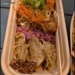 A container filled with various foods, including a sandwich, carrots, and other items.