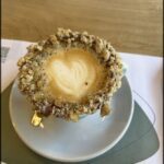 A cup of coffee with a heart shaped cookie on top.