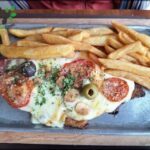 A delicious meal of meat, tomatoes, olives, and french fries.