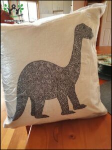A dinosaur pillow sits on a wooden table.
