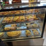 A display case filled with a variety of food items, including pizza, sandwiches, and pastries.