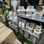 A display of white ceramic sculptures, including a vase and a cup, are arranged on a shelf.