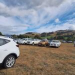 A field full of cars and people, with a beautiful blue sky in the background.