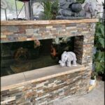 A fish tank with a variety of fish and a small elephant figurine sitting on the edge of the tank.