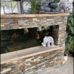 A fish tank with a variety of fish and a small elephant statue sitting on the edge of the tank.