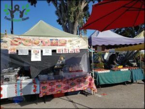 A food stand with a green tent and a red umbrella.