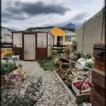 A garden with a variety of flowers and plants, including a potted plant with a yellow house.