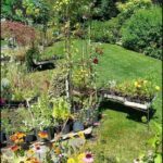 A garden with a variety of flowers and plants, including a wooden cart filled with potted plants.