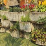 A garden with a variety of plants, including red flowers, is displayed in a stone planter.