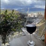 A glass of red wine sits on a table, overlooking a beautiful view of the ocean.