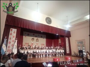 A group of children are standing on stage, waving and smiling at the audience.