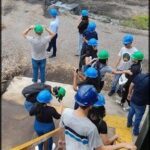A group of construction workers wearing hard hats are standing on a ladder, taking a break and looking at their cell phones.