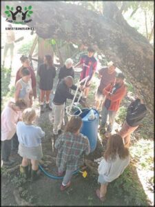 A group of people are gathered around a blue barrel, possibly discussing or working on a project.