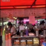 A group of people are gathered around a food stand, ordering and enjoying their meals.