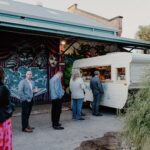 A group of people are gathered around a food truck, which is parked in front of a building with graffiti on it.
