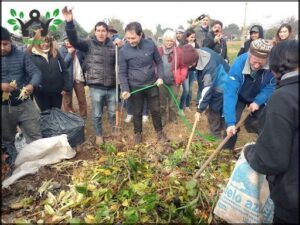 A group of people are gathered around a pile of vegetables, with some of them holding green hoses.