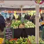 A group of people are gathered around a produce stand, browsing the fresh fruits and vegetables.
