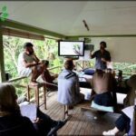 A group of people are gathered around a table, engaged in a presentation.