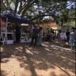 A group of people are gathered around a tent, possibly at a market or event.