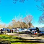 A group of people are gathered in a field, with a variety of vehicles and tents set up.