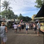 A group of people are gathered in a parking lot, with some of them taking pictures of a food truck.