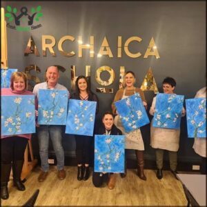 A group of people are posing with their artwork, proudly displaying their flower paintings.