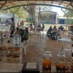 A group of people are sitting at tables under a covered area, enjoying a meal together.